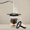 Cohoma PureBrew Filter with steaming hot water pouring over coffee grounds into a glass mug, showcasing the brewing process on a neutral beige background