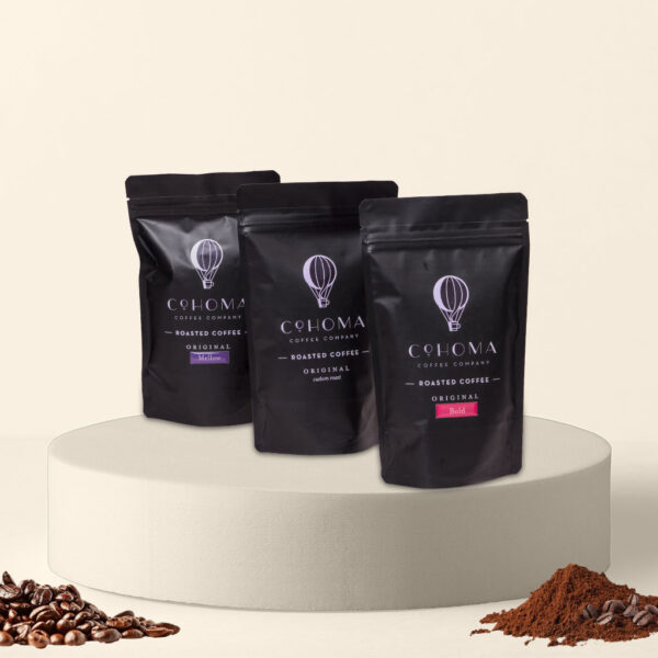 Front view of three Cohoma Coffee variety packs showcasing Mellow, Custom Roast, and Bold options in sleek black packaging with AA+ grade Arabica beans.