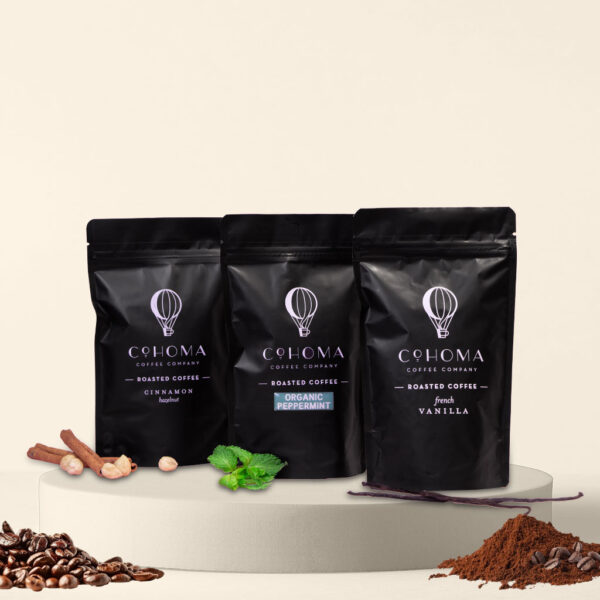 Front view of three Cohoma Roasted Coffee pouches featuring Cinnamon Hazelnut, Organic Peppermint, and French Vanilla flavors, neatly displayed with fresh ingredients around.