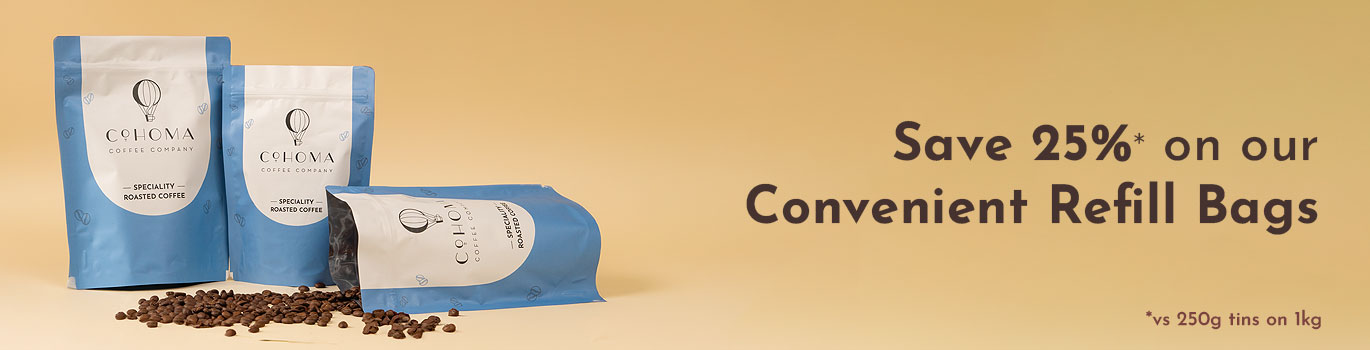 Promotional banner for Cohoma Coffee showcasing blue refill bags of specialty roasted coffee with scattered coffee beans on a beige background