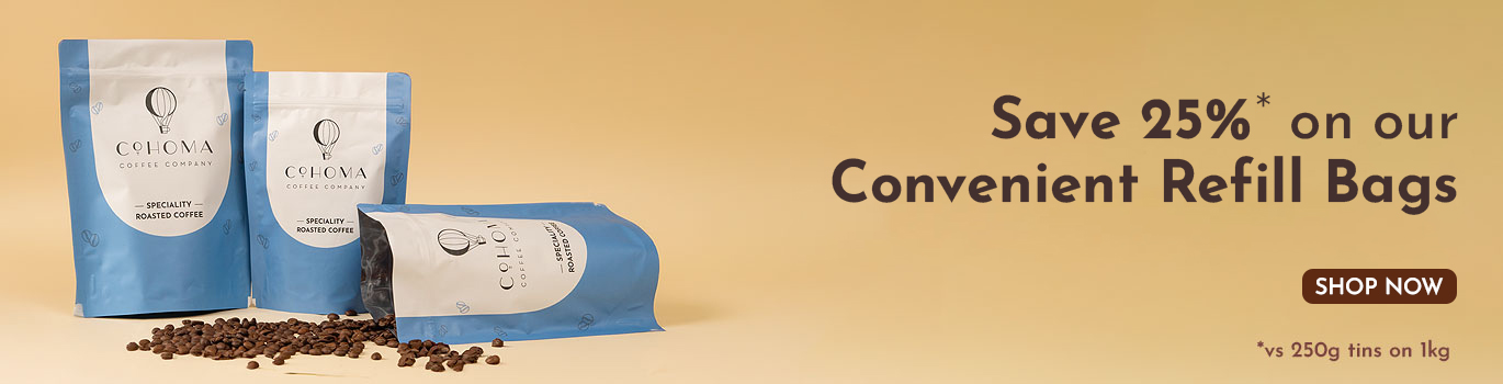 Promotional banner for Cohoma Coffee showcasing blue refill bags of specialty roasted coffee with scattered coffee beans on a beige background