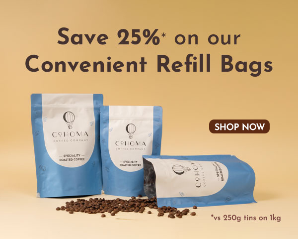 Promotional banner for Cohoma Coffee showcasing blue refill bags of specialty roasted coffee with scattered coffee beans on a beige background